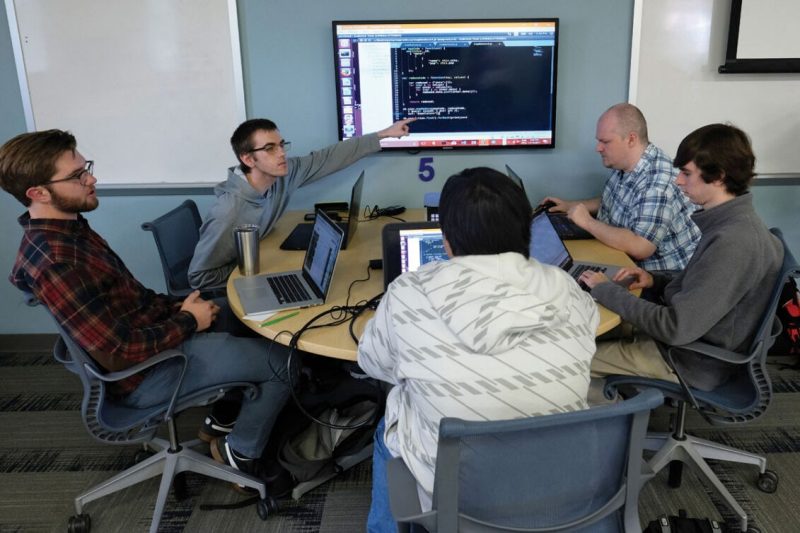 Students and instructors discuss computer code displayed on screen