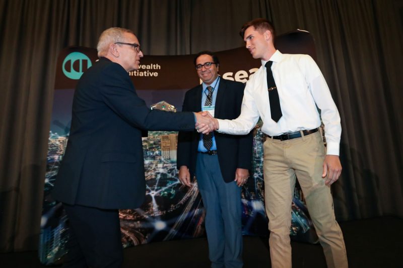 Luiz DaSilva  executive director commonwealth cyber initiative, presents award to VMI team on stage at CCI Symposium