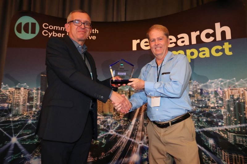 Luiz DaSilva presents Carl Elks with award on stage at CCI Symposium 2023