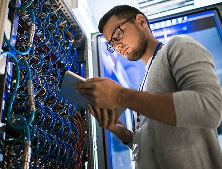 Young man works on digital tablet in front of server cabinet