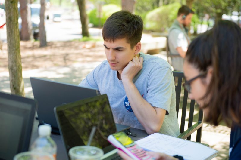 A male student working from a laptop outside.