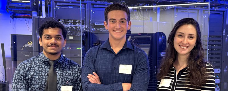 Three people standing in a technology lab with server racks in the background.