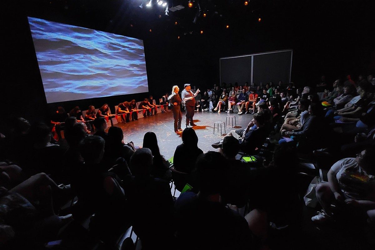 People on stage in front of screen surrounded by audience