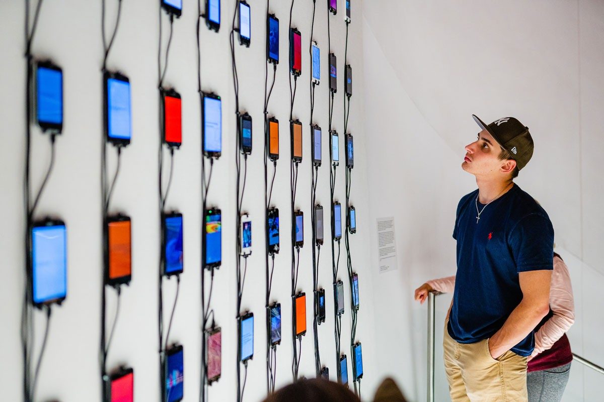 Exhibit goers look at cellphones mounted on wall