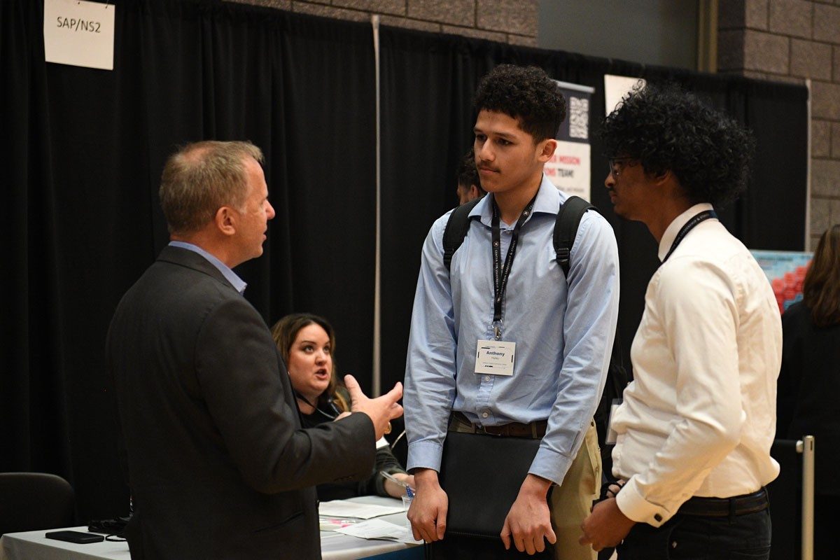 Students talk to a company representative near the SAP NS2 booth at Cyber Fusion 2024