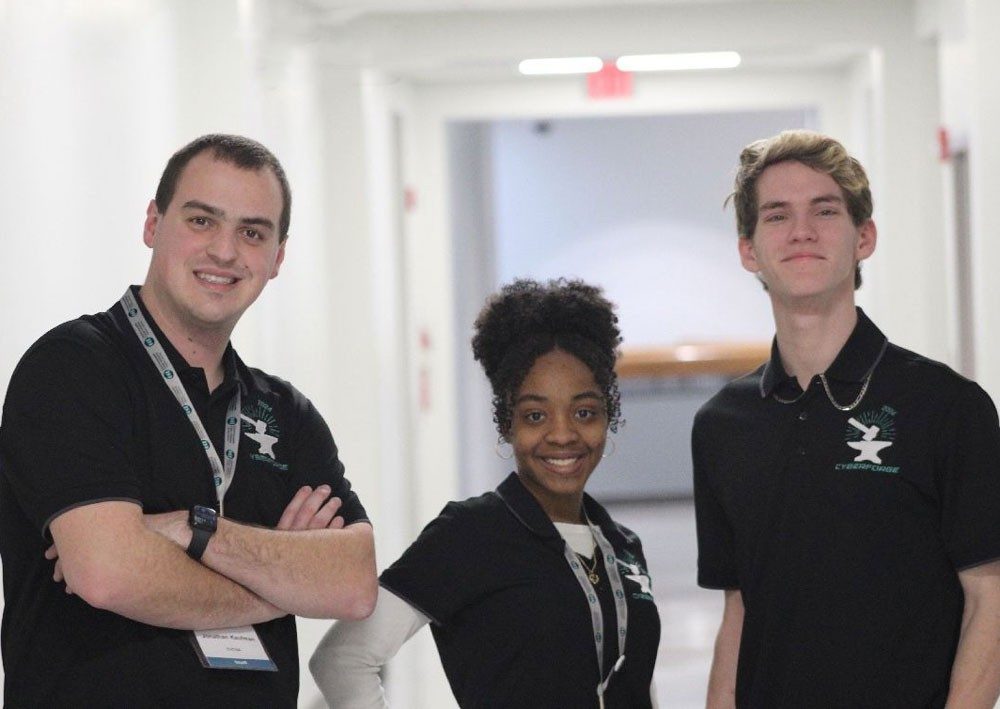 Three students in badges and CyberForge logo shirts