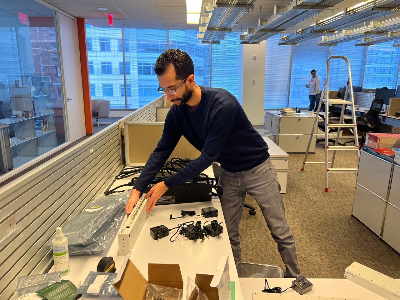 A person stands at a workstation in an office assembling electronic equipment.