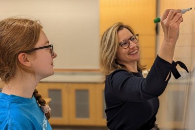 Student with teacher writing on white board