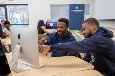 Two young men point at computer screen with ODU logo behind them